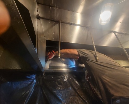 Image of a kitchen hood exhaust being cleaned by a professional.